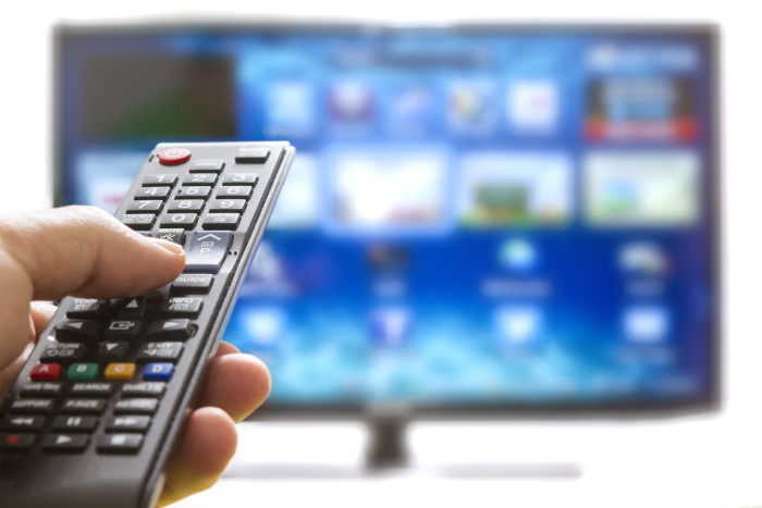 Television remote control changes channels thumb on the blue TV screen